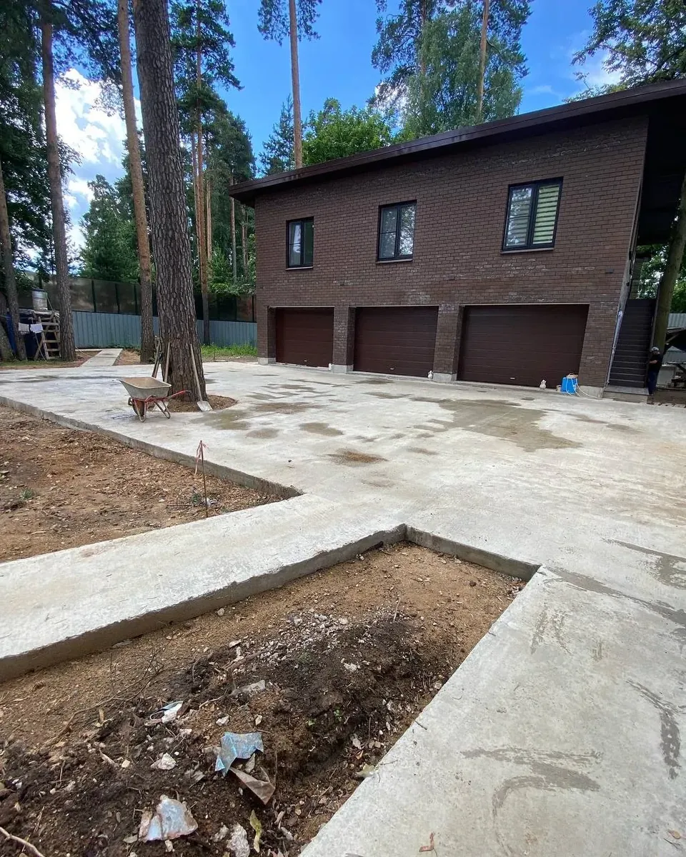 Дорожки и площадка перед кирпичным домом с тремя тёмными гаражными воротами