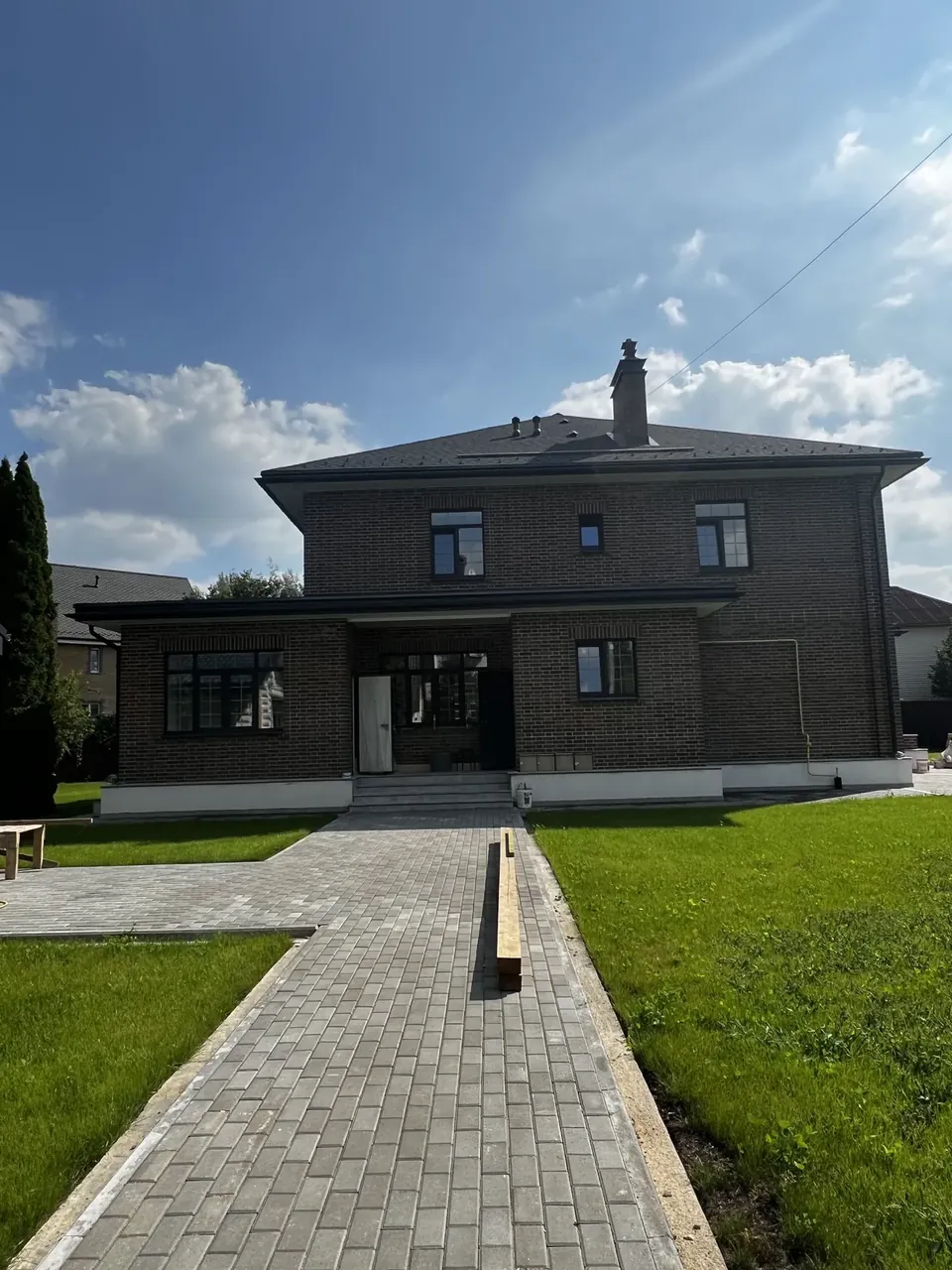 Дорожка из серой плитки, уложенной вразбежку, ведёт к дому с тёмным фасадом
