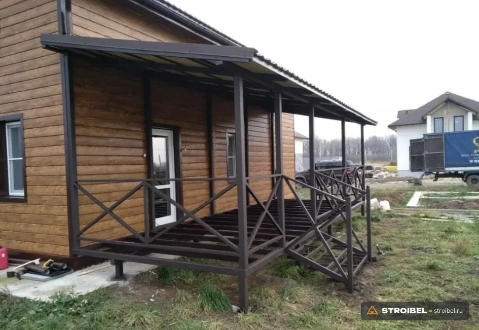 Навес из профлиста на тёмных металлических стойках вдоль стены дома